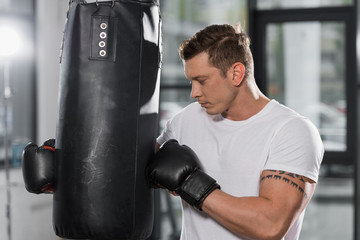 tattooed muscular boxer holding punching bag in gym