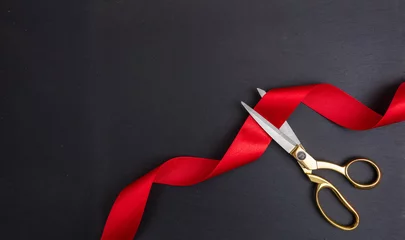 Fotobehang Scissors cutting red silk ribbon against black background © Rawf8