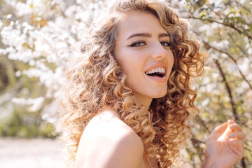 Smiling spring curly girl. Sensual blonde in Blooming flowers in orchard. Spring day concept. Good day.