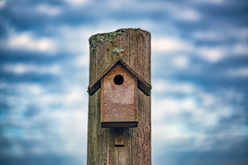Picture of old wooden bird house with dramatic blue sky ath the background