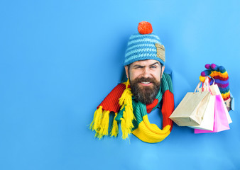 Bearded man in warm clothes holds shopping bags. Man with shopping bags looking through hole on paper. Gift and present. Sale, discount, fashion, retail, consumer, advertisement, black friday concept.