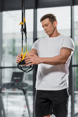 Fototapeta na wymiar handsome athletic bodybuilder holding suspension straps in gym