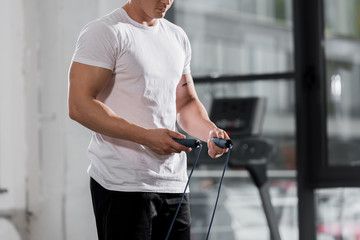 cropped image of athletic bodybuilder standing with jumping rope in gym