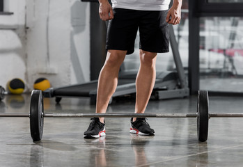 Fototapeta na wymiar cropped image of athletic bodybuilder standing near barbell in gym