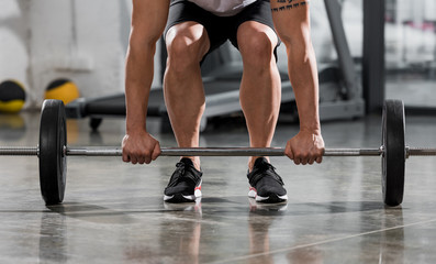 Fototapeta na wymiar cropped image of athletic bodybuilder lifting barbell in gym