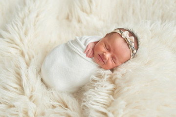 Cute newborn baby girl lies swaddled in a white blanket. Baby goods packaging template. Closeup portrait of newborn baby with smile on face. Healthy and medical concept. 