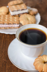 Cup of hot coffee with pastry. Dark wooden background.