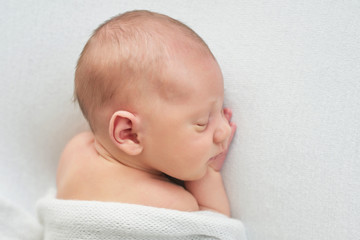 Cute newborn baby lies swaddled in a white blanket. Baby goods packaging template. Closeup portrait of newborn baby with smile on face. Healthy and medical concept. 