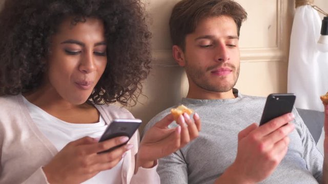 Couple using mobile phone while eating croissant at home