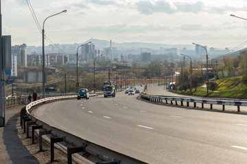 Urban transport rides along Igarskaya Street, against the background of the city of Krasnoyarsk in the spring afternoon.