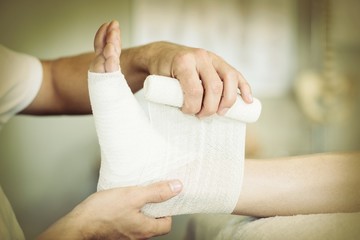 Physiotherapist putting bandage on injured feet of patient