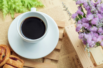 Top view of white cup of black coffee or tea on wooden plate over blurred coffee bean with nature sun lighting.