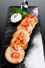 cheese pancakes decorated with strawberry slices with sour cream on a dark background. spase. close up