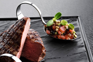 Beautiful serving of a cut steak with vegetables on a black plate on a dark background. Close up
