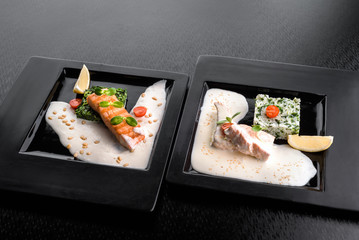 Serving a dish Salmon fillet in a creamy sauce with spinach, lemon and sprouts of soy on a black plate on a dark background. close up. isolated