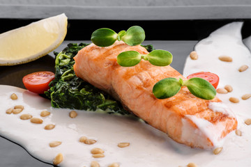 Serving a dish Salmon fillet in a creamy sauce with spinach, lemon and sprouts of soy on a black plate on a dark background. close up. isolated