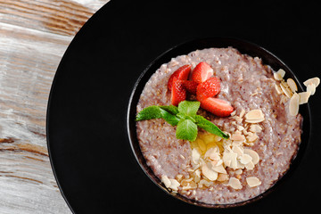 oatmeal with wild berries and nuts decorated with mint in a black plate on a dark background. top view. close up. macro