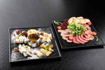 cold smoked meat plate with pork chops, prosciutto, salami and bread sticks on a black plate on a dark background