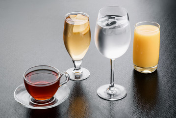 Transparent cup of tea, lemonade, glass of ice water and orange juice isolated on a dark background. close-up.