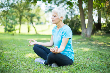 Obraz premium Senior woman in a lotus position on a grass