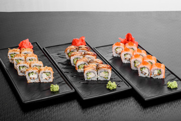 Maki Sushi set on dark pattern background. Sushi Set nigiri, rolls and sashimi served in black square plate. On dark pattern background.