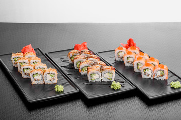 Maki Sushi set on dark pattern background. Sushi Set nigiri, rolls and sashimi served in black square plate. On dark pattern background.