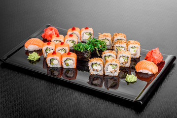 Maki Sushi set on dark pattern background. Sushi Set nigiri, rolls and sashimi served in black square plate. On dark pattern background.