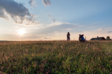 Variety and diversity of colors during golden hour in nature; Two photographers, man and woman, take pictures of meadow flowers and grass at sunset. Evening sky and rural landscape