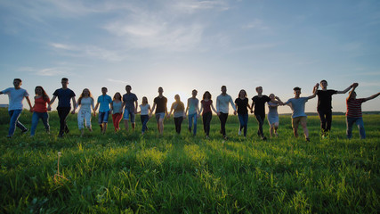 Silhouettes of nineteen friends holding hands on a sunset background.