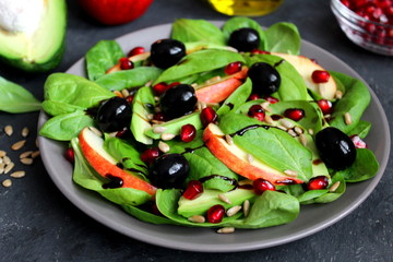Fresh salad with spinach, avocado, apple, pomegranate and sunflower seed on dark background. Top view with copy space.