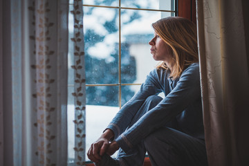 Sad woman sitting by the window looking outside