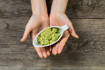 Beautiful woman hands holding grave boat with guacamole sauce on wooden background top view closeup