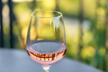 Shiny clean wine glass with pink-coloured rose wine reflecting spears of a surrounding fence standing on a gray table in a cafe outside shot in the afternoon in natural light