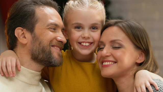 Girl kissing mom and dad on cheeks, showing love and care to family on Christmas