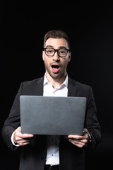 emotional young businessman with laptop looking at camera isolated on black