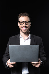 smiling young businessman with laptop looking at camera isolated on black