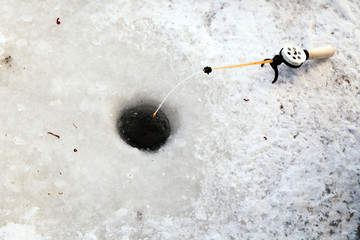 Hole in the ice for winter fishing and a fishing rod with a reel and fishing line and bait. Concept...