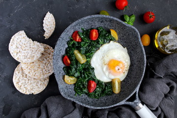 Fried eggs with spinach and tomato on iron pan. Healthy breakfast. Top view with copy space. © Ale02