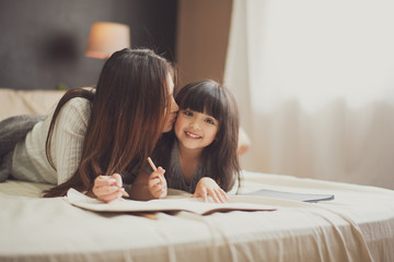 Love of young mother and daughter. Teaching reading a homework or book on the bed at home. mother...