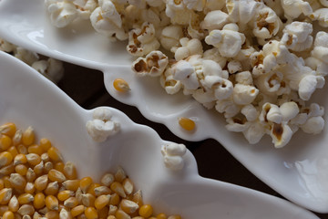 popcorn and popcorn grains on white plate on wooden background