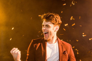 celebrating young man under falling confetti on black