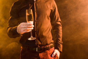 cropped shot of man with glass of champagne under yellow light on black