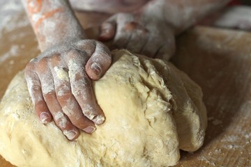 Fototapeta premium The hands of a girl or daughter knead the dough in the kitchen on a wooden board