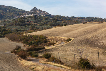 The curved country road through arable fields to the medieval castle-town in Tuscany, Italy