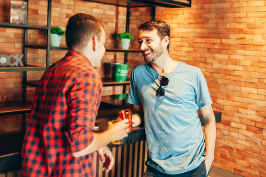 Two Men In Casual Clothes Having A Conversation At Bar Counter In Pub