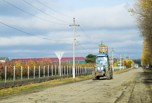 The tractor rides on the asphalt of the village street. Autumn village in Russia