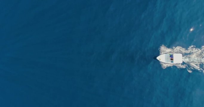 Aerial drone top shot over small white boat sailing in the middle of the sea with young woman in purple lying on a sunny day