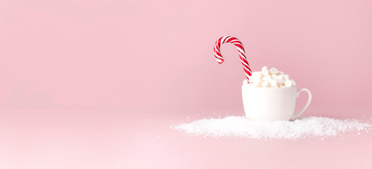 Christmas New Year drink, white mug with marshmallows and Candy Cane in the snow on pink background...