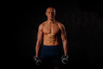 Fototapeta na wymiar Handsome muscular man working out with dumbbells over black background.
