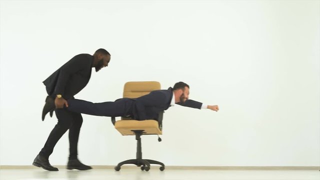 The two happy businessmen playing with an office chair. slow motion